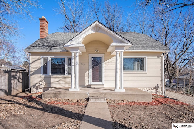 bungalow-style home with a shingled roof, a chimney, and fence