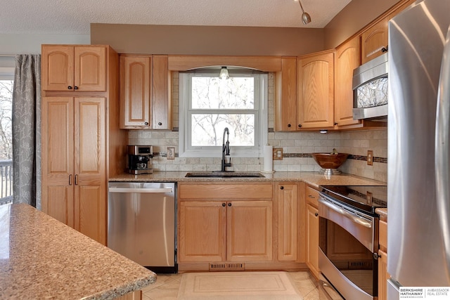 kitchen with stainless steel appliances, a sink, visible vents, light brown cabinetry, and tasteful backsplash