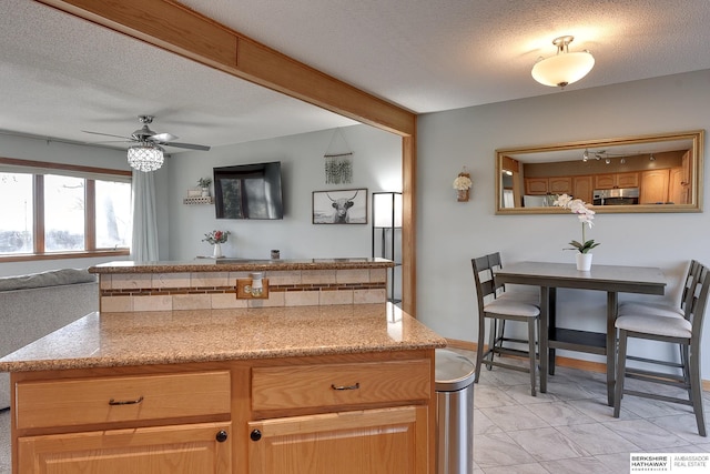 kitchen featuring open floor plan, light stone counters, a textured ceiling, and a ceiling fan