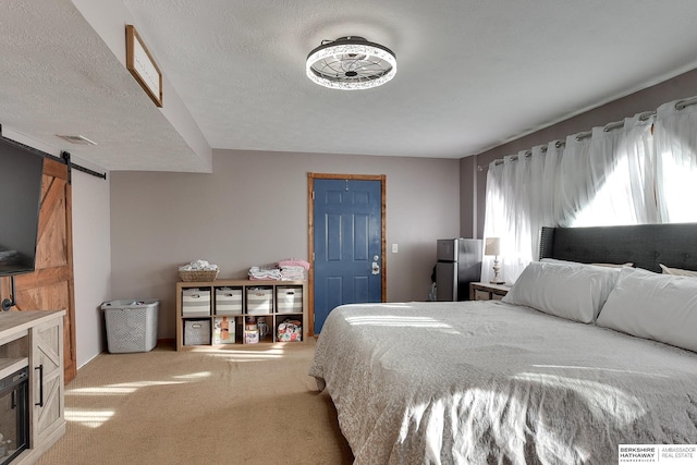 carpeted bedroom featuring a barn door, visible vents, a textured ceiling, and freestanding refrigerator