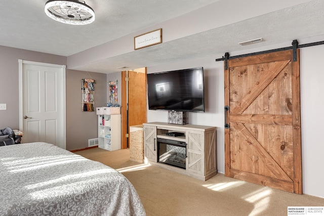 carpeted bedroom featuring a barn door, visible vents, and a textured ceiling