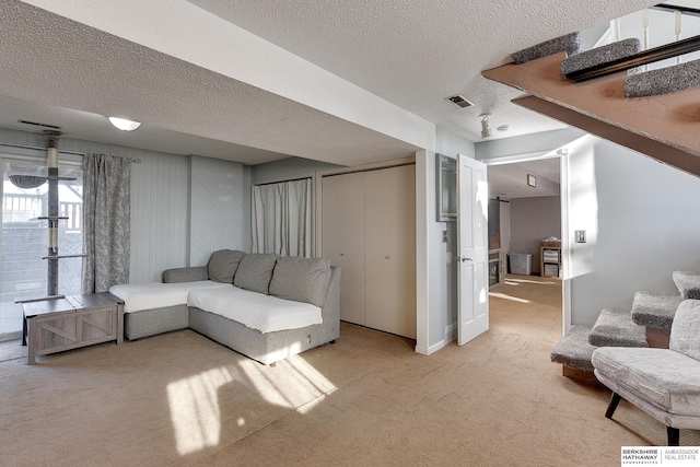 living room featuring light carpet, stairs, visible vents, and a textured ceiling