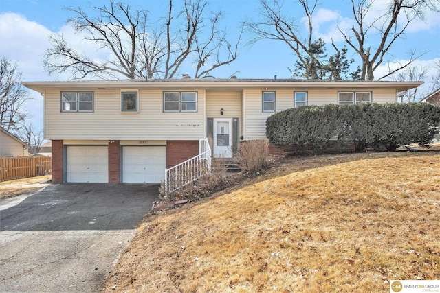 raised ranch featuring brick siding, a front yard, fence, a garage, and driveway