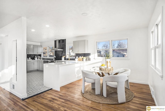 kitchen with wall chimney range hood, decorative backsplash, gray cabinets, and wood finished floors