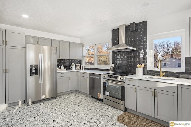 kitchen featuring wall chimney exhaust hood, appliances with stainless steel finishes, gray cabinets, and a sink