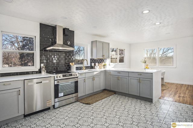 kitchen featuring stainless steel appliances, wall chimney exhaust hood, a sink, and gray cabinetry