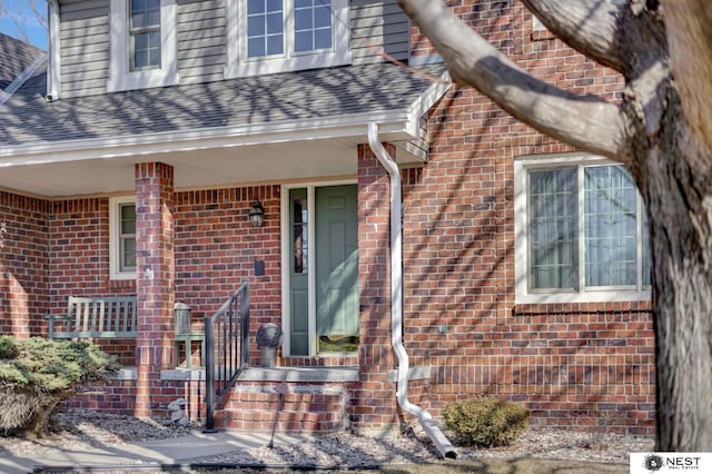 view of exterior entry featuring a shingled roof and brick siding