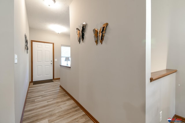 hallway featuring baseboards, a textured ceiling, and light wood finished floors