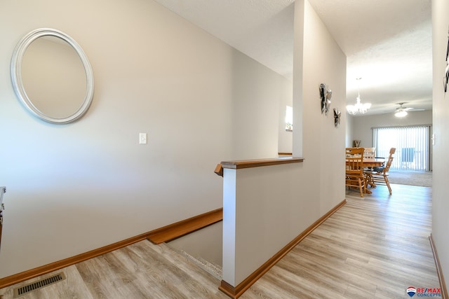 hallway featuring light wood finished floors, baseboards, visible vents, and an upstairs landing