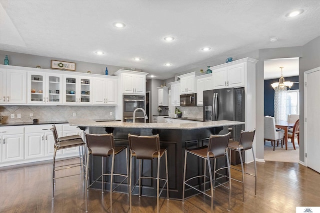 kitchen featuring an island with sink, dark wood-style floors, appliances with stainless steel finishes, a breakfast bar area, and white cabinetry