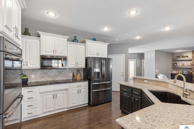 kitchen featuring light stone counters, appliances with stainless steel finishes, dark wood-type flooring, white cabinets, and a sink