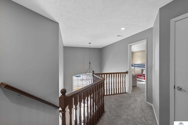 corridor featuring carpet, visible vents, a textured ceiling, and an upstairs landing