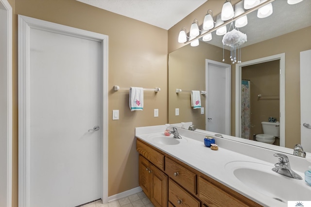 bathroom with double vanity, a sink, toilet, and baseboards