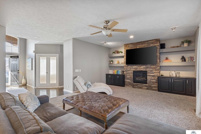 living area with built in shelves, baseboards, a textured ceiling, and a stone fireplace