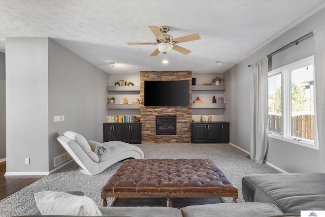 living room with a textured ceiling, a stone fireplace, visible vents, and baseboards