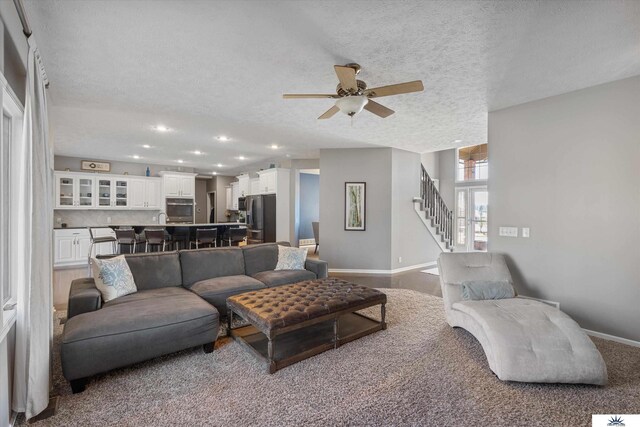 living area with stairs, ceiling fan, a textured ceiling, and baseboards