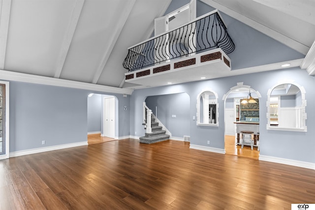 unfurnished living room with baseboards, arched walkways, stairway, wood finished floors, and high vaulted ceiling