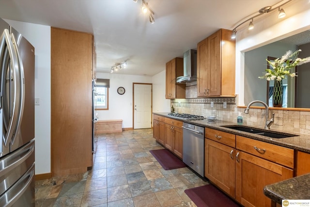 kitchen with stainless steel appliances, a sink, wall chimney range hood, backsplash, and brown cabinets