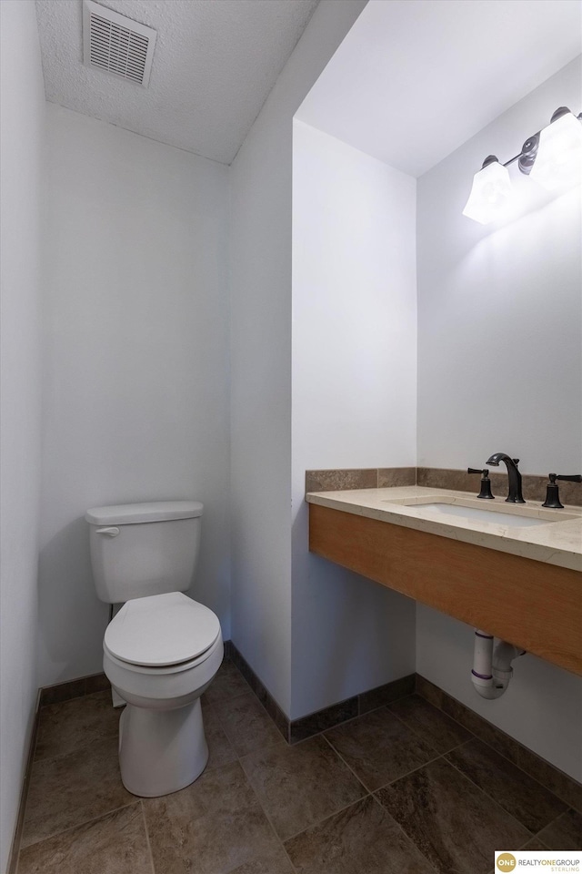 bathroom with tile patterned flooring, toilet, a sink, visible vents, and baseboards