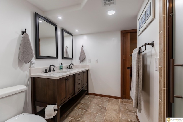 bathroom with toilet, double vanity, visible vents, and a sink