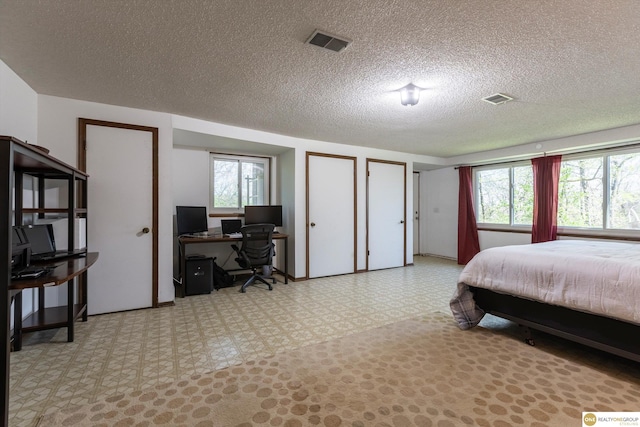 bedroom featuring a textured ceiling, multiple closets, visible vents, and tile patterned floors