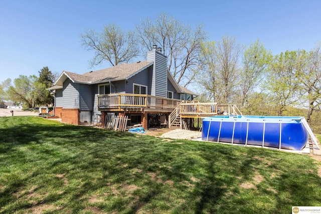 back of property featuring an outdoor pool, a lawn, a chimney, a wooden deck, and brick siding