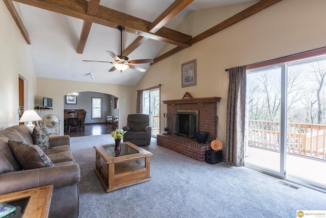 carpeted living area featuring visible vents, arched walkways, beamed ceiling, a fireplace, and high vaulted ceiling