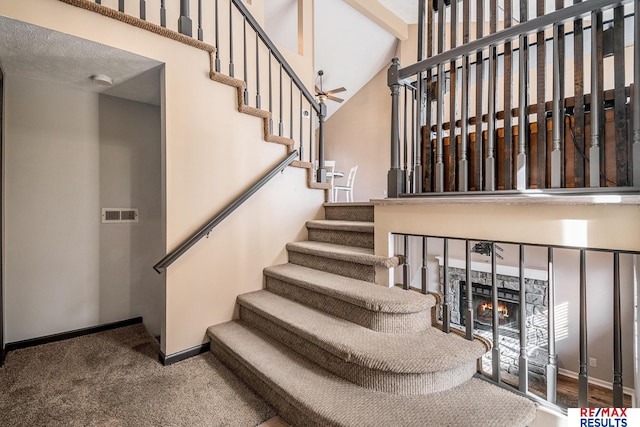 staircase featuring visible vents, carpet flooring, a fireplace, baseboards, and ceiling fan