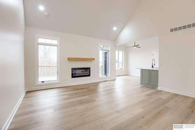 unfurnished living room with a glass covered fireplace, visible vents, plenty of natural light, and light wood finished floors