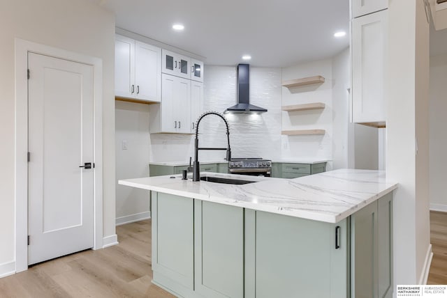 kitchen with light wood-type flooring, wall chimney range hood, decorative backsplash, and a sink