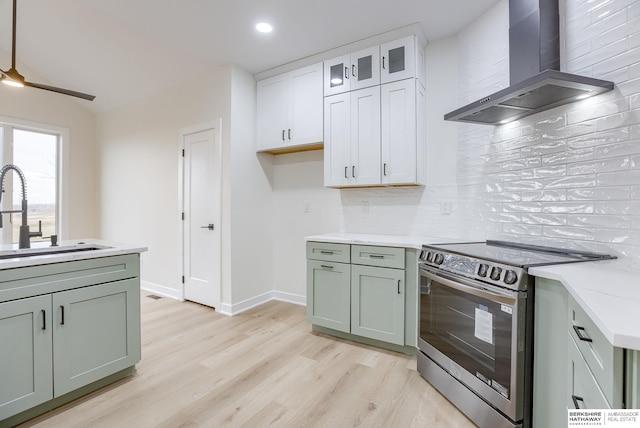 kitchen with stainless steel electric range oven, light wood-style flooring, backsplash, a sink, and wall chimney range hood