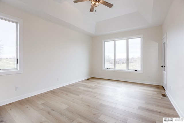 empty room featuring ceiling fan, visible vents, baseboards, light wood finished floors, and a raised ceiling