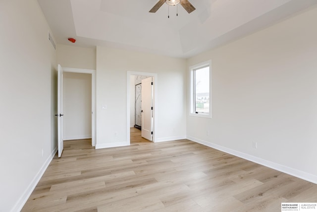 unfurnished bedroom with visible vents, a tray ceiling, light wood-style flooring, and baseboards