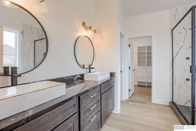 full bath featuring double vanity, a sink, a marble finish shower, and wood finished floors