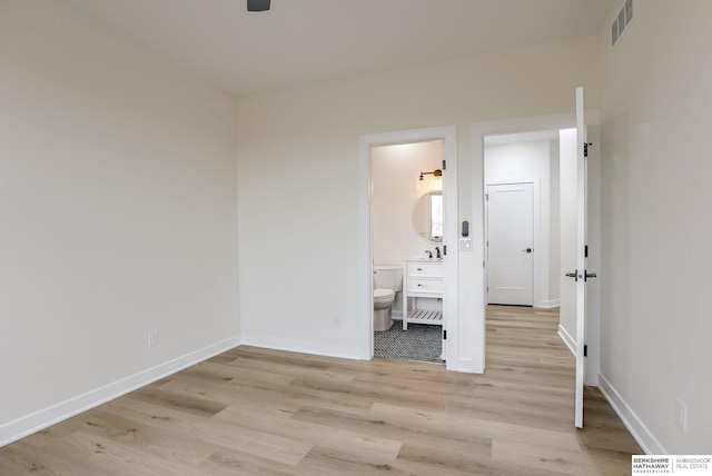 unfurnished bedroom featuring baseboards, ensuite bath, visible vents, and light wood-style floors