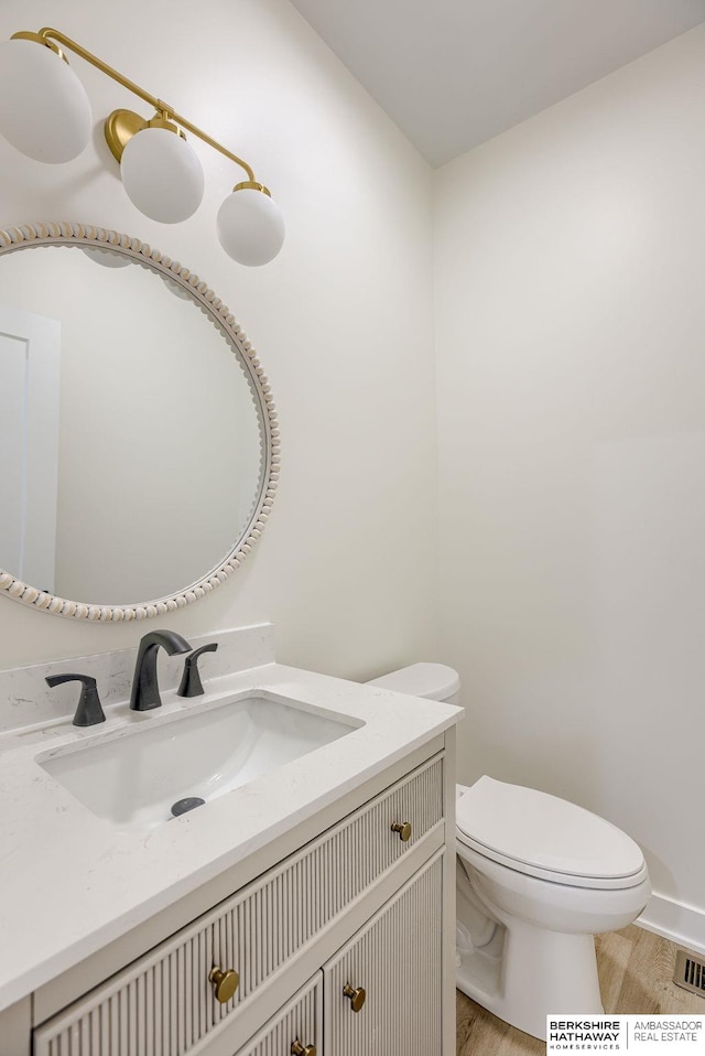 half bathroom featuring visible vents, vanity, toilet, and wood finished floors