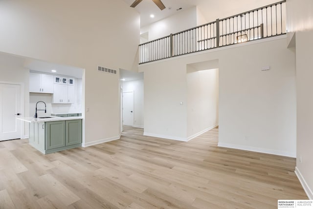 unfurnished living room with light wood-style floors, visible vents, ceiling fan, and baseboards