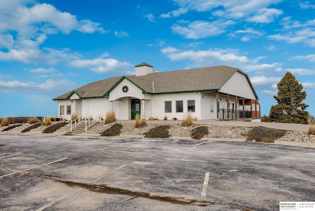 ranch-style home featuring uncovered parking and roof with shingles