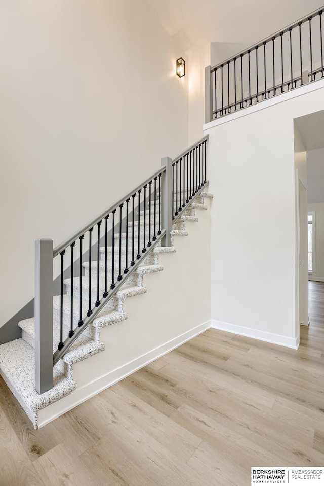 stairway with baseboards, a high ceiling, and wood finished floors