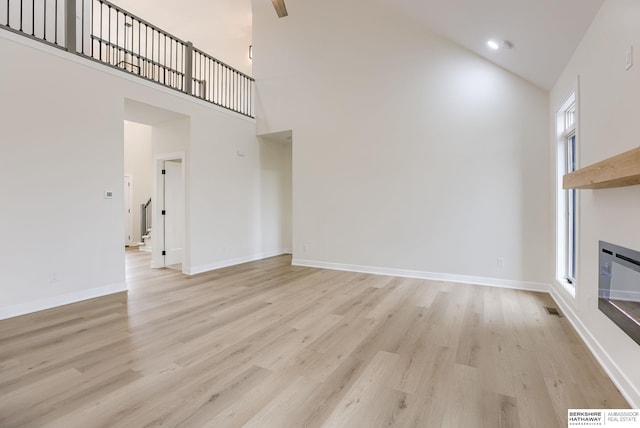 unfurnished living room with light wood-style floors, baseboards, and a high ceiling