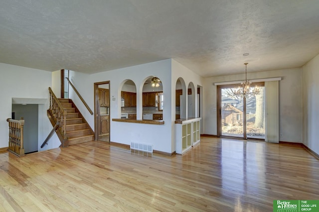 unfurnished living room with visible vents, a textured ceiling, stairway, light wood-style floors, and an inviting chandelier