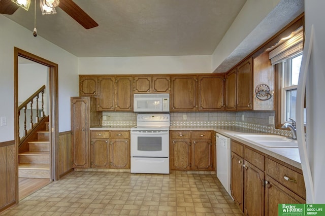 kitchen with a sink, white appliances, brown cabinetry, and wainscoting