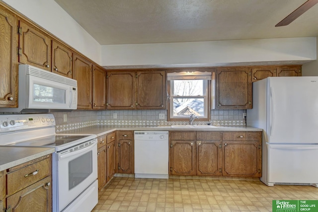 kitchen featuring light floors, white appliances, brown cabinets, and a sink