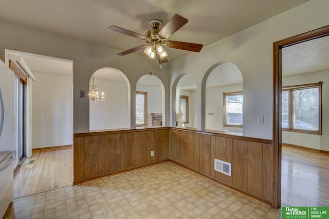 kitchen featuring visible vents, wooden walls, light floors, wainscoting, and brown cabinetry