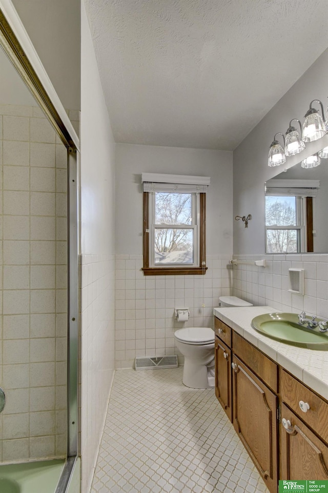 bathroom with tile walls, an enclosed shower, a healthy amount of sunlight, and a textured ceiling