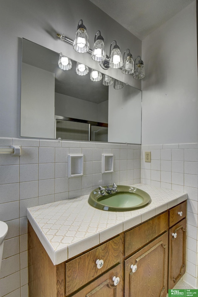 bathroom with a shower with shower door, toilet, tile walls, and vanity