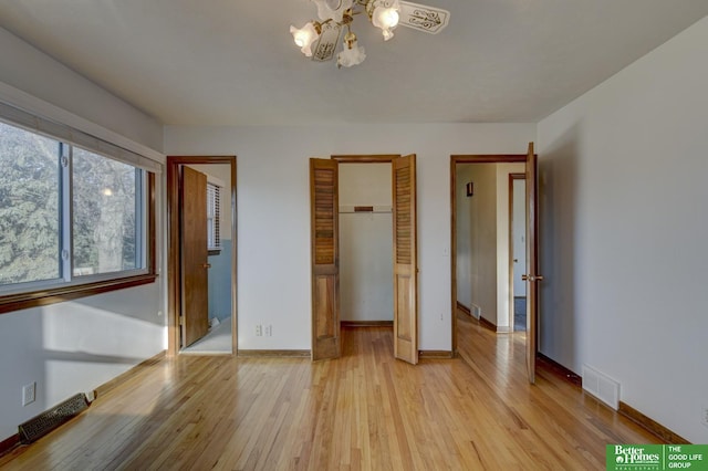 unfurnished bedroom with visible vents, baseboards, a chandelier, and light wood finished floors