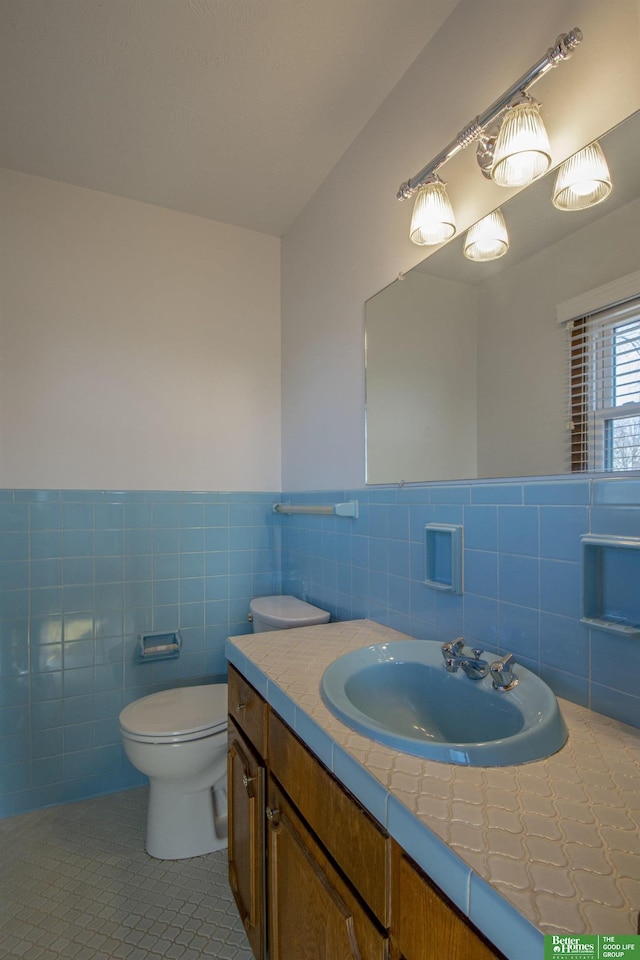 bathroom featuring tile patterned flooring, tile walls, toilet, wainscoting, and vanity