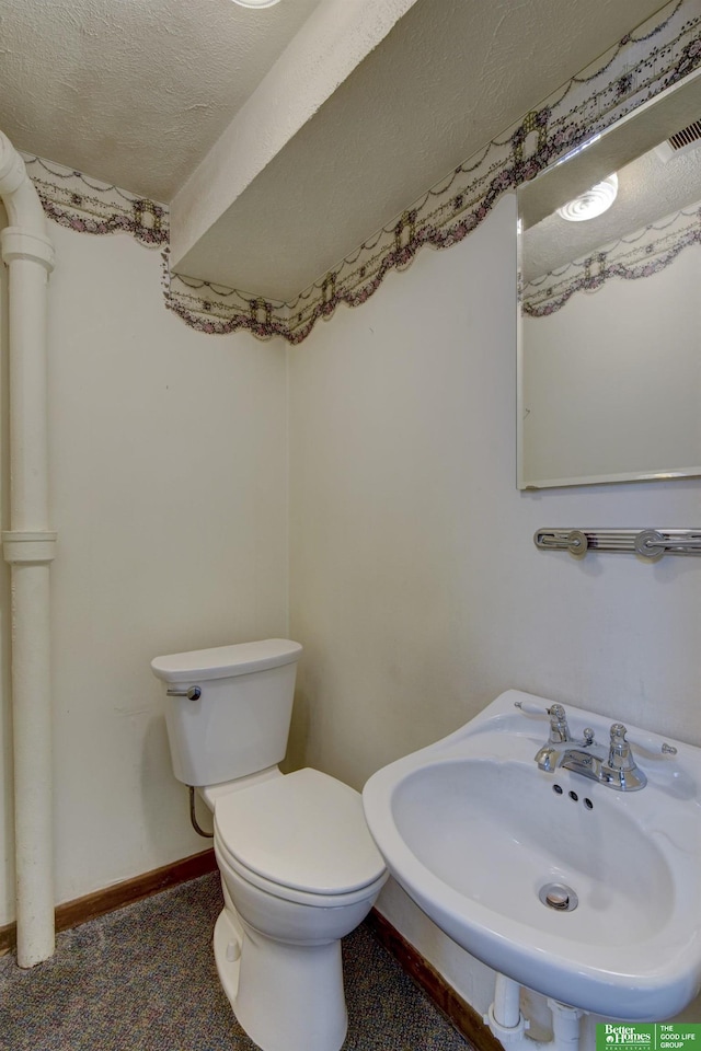 half bathroom with a textured ceiling, toilet, baseboards, and a sink