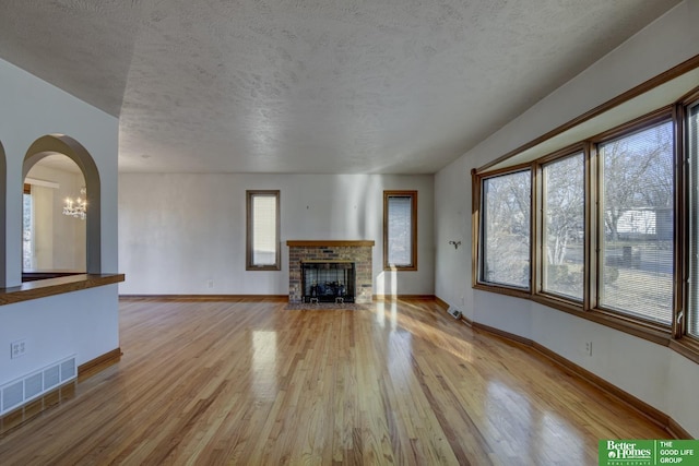 unfurnished living room with visible vents, a textured ceiling, a brick fireplace, and wood finished floors